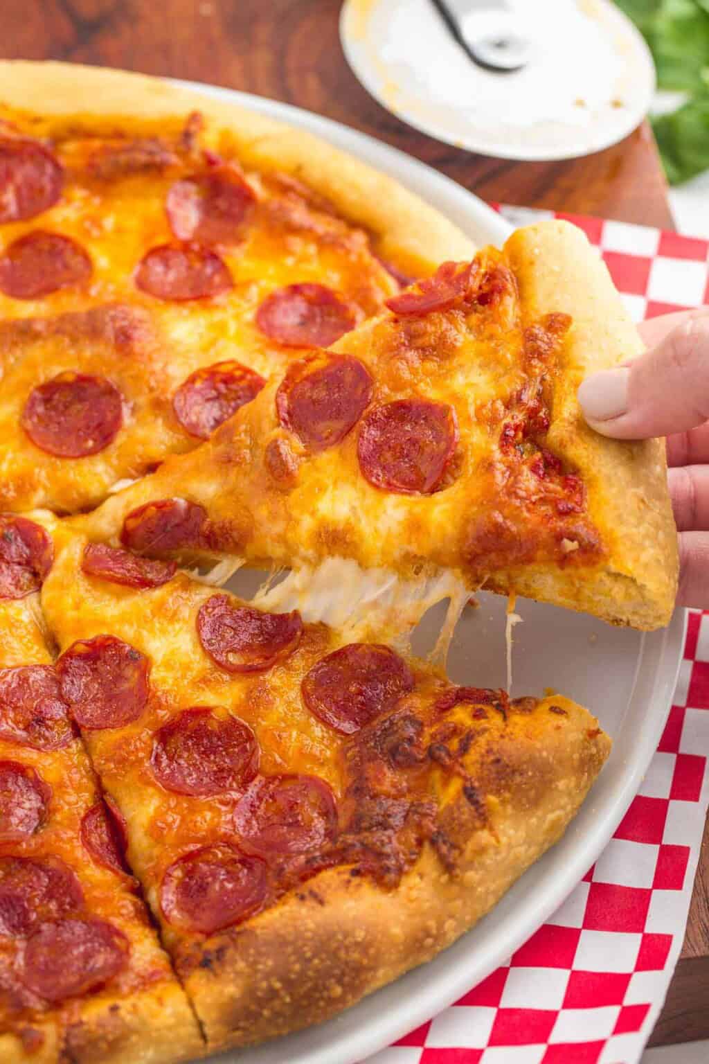 A tall slice of extra cheesy homemade pepperoni pizza with a thick golden crust and layers of melted cheese